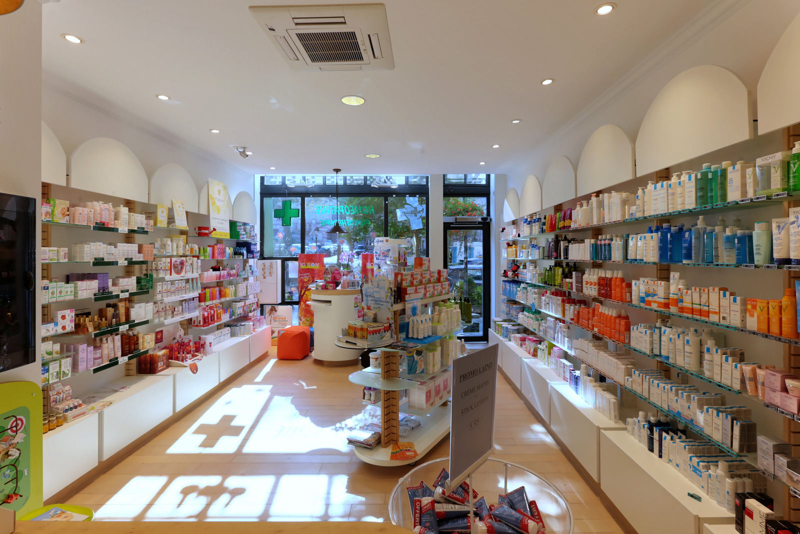 Intérieur de la pharmacie avec la croix de pharmacie projetée par le soleil sur le sol.